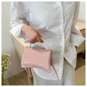 Close-up of light pink handbag featuring pearl handle and unique curved base design