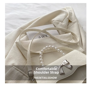 Cream crossbody bag detail with pearl handle and metal butterfly clasp on a blazer