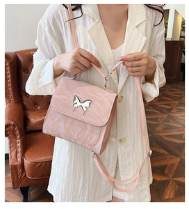 Pink patent leather handbag with a silver butterfly buckle shown in a cozy home setting