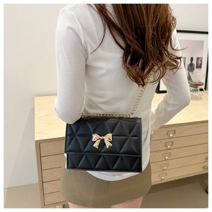 Macro view of black quilted faux leather crossbody bag with golden bow clasp