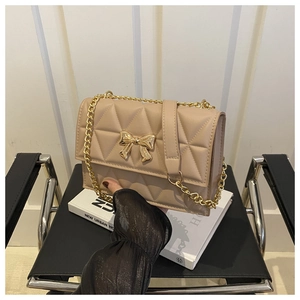 Detail of beige quilted shoulder bag with golden bow buckle and chain strap