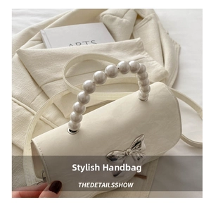 Close-up of cream glossy leather handbag featuring pearl handle and silver bow detail