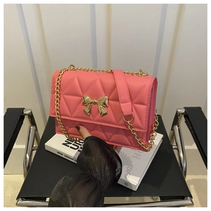 Detail of pink quilted crossbody bag with golden bow clasp and metal chain strap