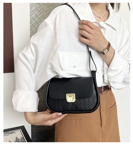 Detail of a black quilted leather crossbody bag with a gold square lock on a female model