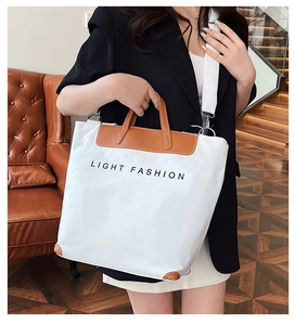 Detailed close-up of white canvas tote bag with brown leather handles and side straps
