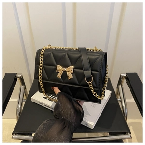 Close-up of black quilted shoulder bag featuring a polished gold metal bow detail