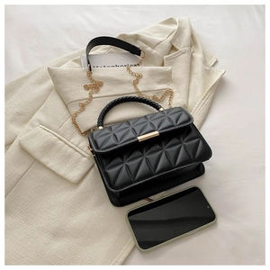 Detail of black quilted leather crossbody bag featuring gold hardware and woven handle