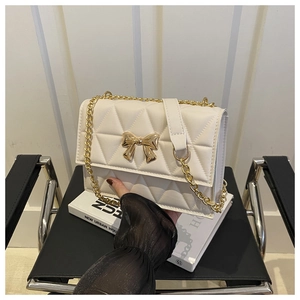 Detail of white quilted handbag with gold metal bow and elegant chain strap