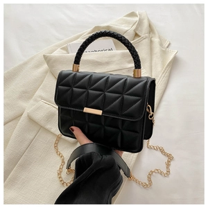 Detail of black quilted crossbody bag with gold hardware on a beige blazer