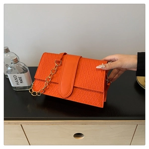 Detail of orange flap bag featuring triangular embossing and gold metal chain strap