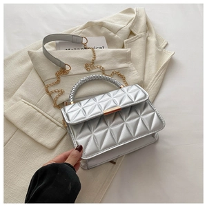 Detailed view of silver quilted crossbody bag with gold chain strap on beige blazer