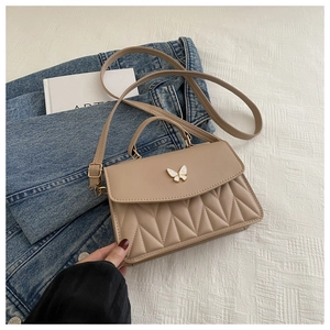 Detail der beige gesteppten Handtasche mit Schmetterlingsschnalle und Perlenakzenten