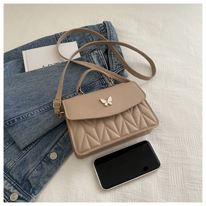 Detail der beigen eckigen Tasche mit Steppmuster und elegantem Schmetterlingsanhänger