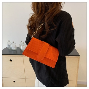 Detail of orange crossbody bag with geometric embossed pattern and gold chain strap