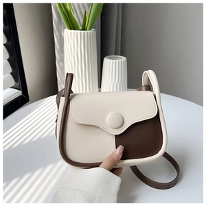 Detail view of retro cream and brown leather crossbody bag on a white table