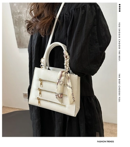 Close-up of white crossbody bag with gold zipper accents and floral silk scarf on handle