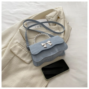 Detail of light blue wave edge bag with pearl handle and metal bow decoration