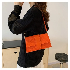 Detail of orange flap handbag featuring geometric embossed texture and gold metal rings