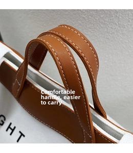 Close-up of the comfortable caramel leather handle on the canvas tote bag with contrast stitching