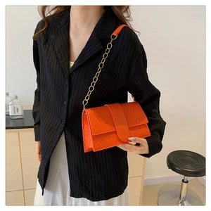 Detail of orange crossbody bag featuring 3D geometric embossed texture and gold chain strap