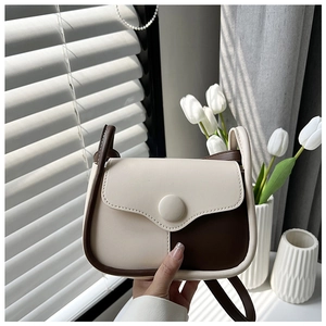 Detail of cream and brown crossbody bag with circular buckle and premium edge stitching