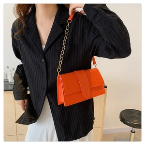 Detail shot of bright orange embossed leather shoulder bag with gold chain strap on model
