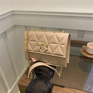 Quilted beige shoulder bag with gold butterfly clasp and chain strap in soft lighting