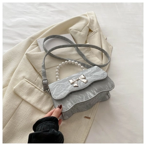 Detail of light gray pleated handbag with silver butterfly knot and pearl handle on a blazer