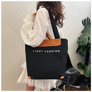 Detailed view of canvas tote bag with Light Fashion text and leather corners on black fabric