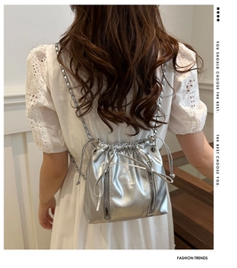 Close-up of metallic silver bucket bag with drawstring closure and chain strap on model