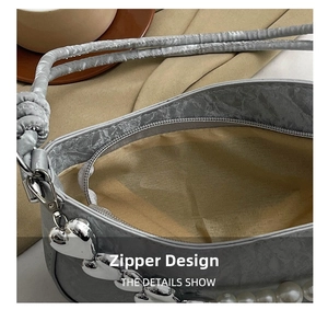 Detail shot of the zip closure with pearl chain and heart charm on a grey ruched handbag