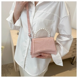 Pink patent leather handbag with pearl handle and curved base, shown in a cozy setting