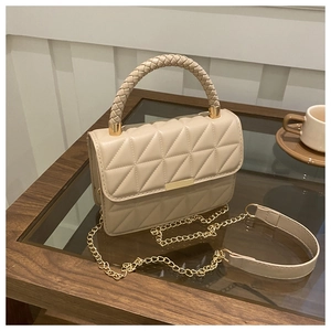 Detail of cream quilted crossbody bag with woven handle and gold hardware on a cafe table
