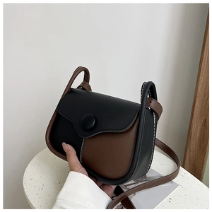 Detail of two-tone saddle bag with matte black button and contrast white stitching