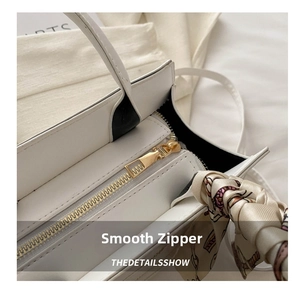 Close-up of smooth gold zipper and printed silk scarf detail on white leather handbag
