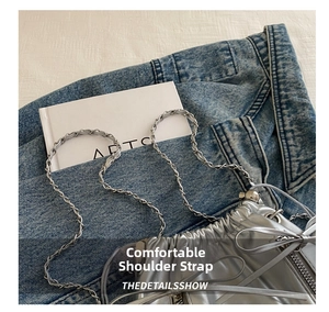 Detail of silver metallic drawstring bucket bag with bow and chain strap on denim