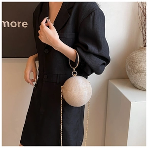 Close-up of champagne gold spherical evening bag with metal ring handle and chain strap