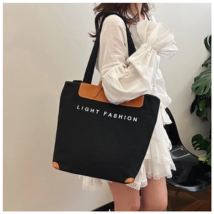 Close-up of black canvas tote bag with brown leather reinforcement and white text