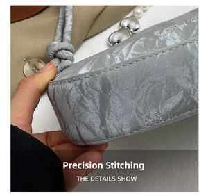 Detail of silver gray shoulder bag showing pleated texture and heart-shaped metal charm