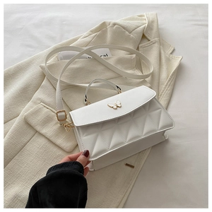 Detail of white quilted crossbody bag with gold butterfly clasp on beige blazer