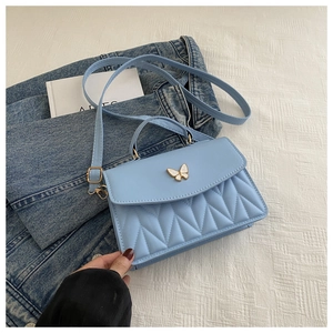Detail der hellblauen Stepphandtasche mit goldenem Schmetterlingsverschluss und Kette