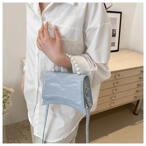 Detail of light blue wrinkled leather handbag with elegant white pearl handle on model