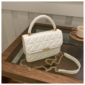 Close-up of white quilted crossbody bag with woven handle and gold hardware on a desk