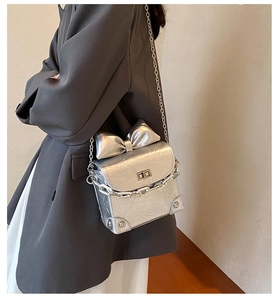 Detail van zilveren mini-tas met grote strik en dubbele metalen kettingriemen