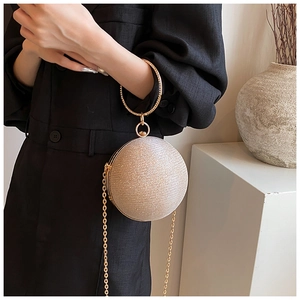 Detail of a golden spherical evening bag with glitter finish and a circular metal handle