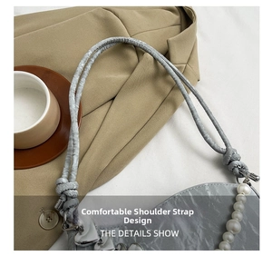 Detail of grey pleated shoulder bag featuring knotted strap, pearl chain and heart charm