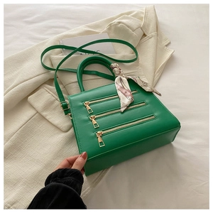 Detail of green leather handbag with triple gold zippers and patterned pink silk scarf