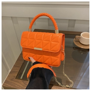 Detail of bright orange quilted leather bag with gold buckle and chain strap on a table