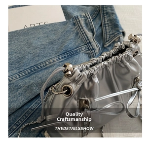 Detail of silver drawstring bucket bag showing metal chain strap and pleated craftsmanship