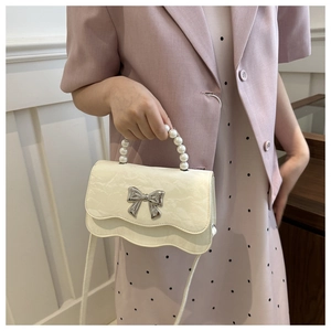 Detail of cream white pleated handbag with pearl handle and silver bow decoration